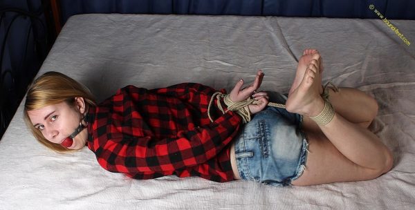 Кавказскую девушку оставляют связанной и с кляпом во рту на кровати в рубашке и шортах
