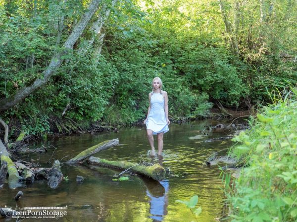 Молодая блондинка Майя плещется водой, стоя голой на коленях в ручье