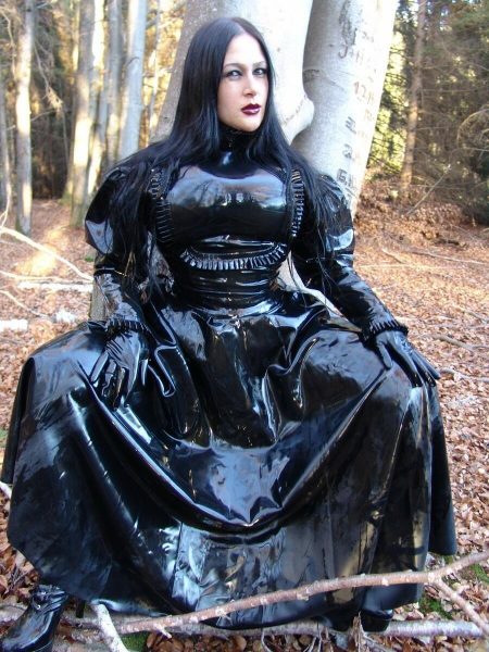 Сольная модель Леди Анджелина позирует полностью одетая в лесу в латексе