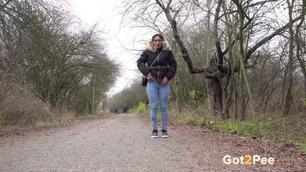 Одинокая девушка Наташа Инк садится на корточки, чтобы пописать на проселочной дороге, одетая в парку