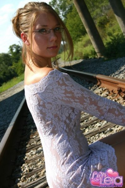 Любительская девушка-одиночка позирует обнаженной на железнодорожных путях в обтягивающем платье и очках