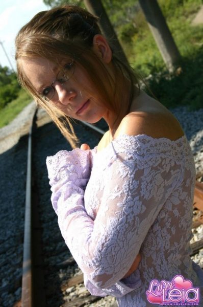 Любительская девушка-одиночка позирует обнаженной на железнодорожных путях в обтягивающем платье и очках