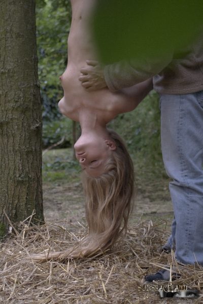 Молодую блондинку дергают за волосы после того, как ее подвесили вверх ногами в лесу