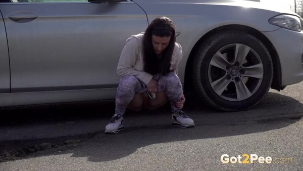 Расстроенная девушка Билли садится на корточки, чтобы отлить рядом с припаркованным автомобилем