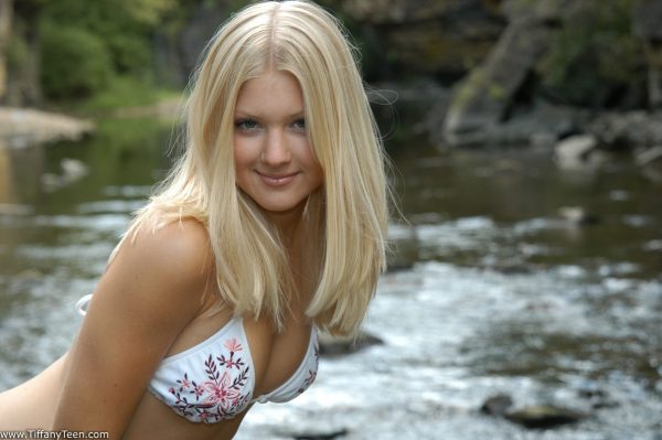 Молодая блондинка Тиффани моделирует на камнях в реке в бикини на завязках