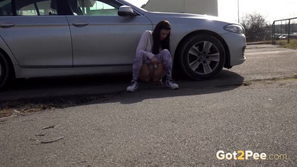 Расстроенная девушка Билли садится на корточки, чтобы отлить рядом с припаркованным автомобилем